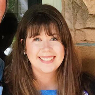 It's a portrait of a young woman with straight brown hair. She has bangs and is smiling as she makes eye contact with the camera